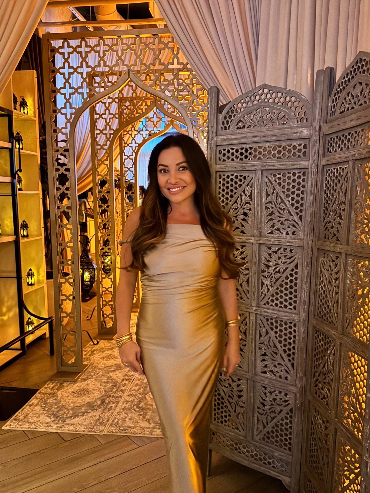 Maddy K in gold satin beside carved screens